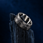 The Midnight black tungsten ring with meteorite inlay resting on charred wood